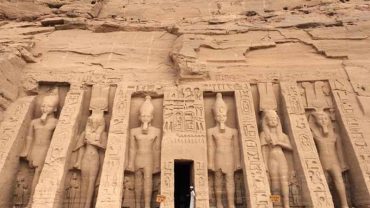 The colossal facade of the Great Temple of Ramesses II at Abu Simbel, carved into a sandstone cliff, with four massive seated statues of the pharaoh guarding the entrance