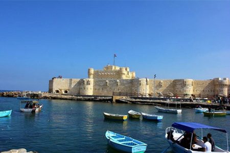The imposing Qaitbay Fortress standing proudly on the coast of Alexandria, with numerous fishing boats and smaller vessels visible in the blue Mediterranean waters below