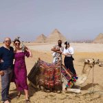 A group of friends smiling and posing cheerfully with camels in front of the majestic Giza Pyramids, indicating a fun and memorable tour experience