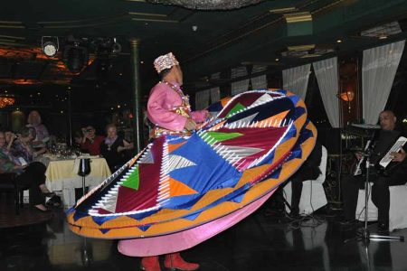 A male Tanoura dancer in a vibrant, multi-layered skirt spinning gracefully on a dinner cruise boat