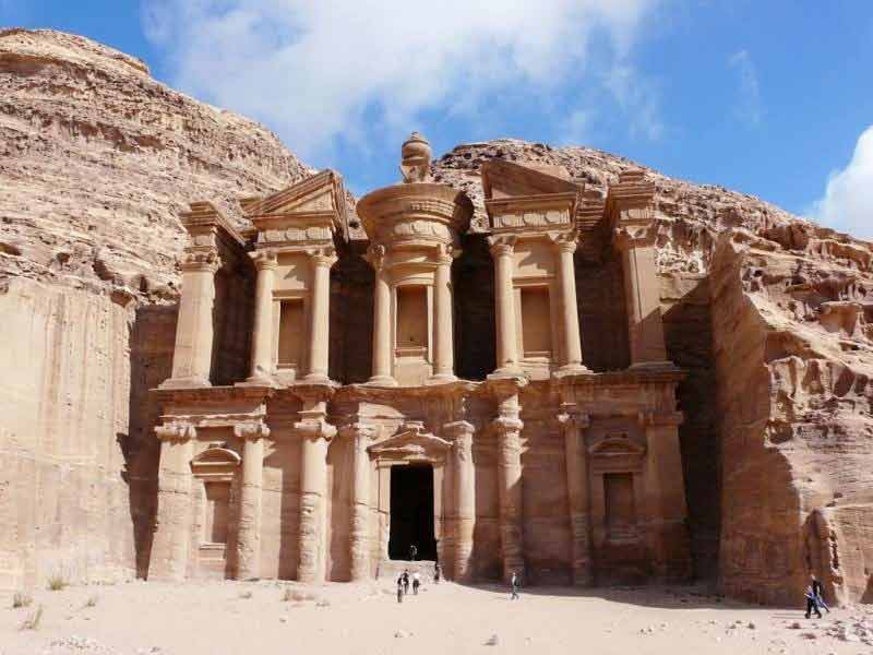 A panoramic view of Petra's vast archaeological site, showing numerous rock-cut tombs, temples, and dwellings carved into the colorful sandstone mountains of the ancient city