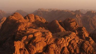 reddish-brown granite peaks of Mount Sinai (Gabal Musa), showing its barren and dramatic desert landscape under a vast sky, evoking its spiritual significance