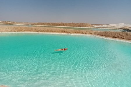 A client effortlessly floating on the highly buoyant, crystal-clear waters of a salt lake in Siwa Oasis
