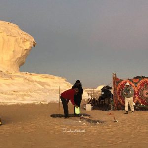 Campement dans le désert avec deux tentes, un véhicule 4x4, des personnes et des formations rocheuses blanches en arrière-plan.